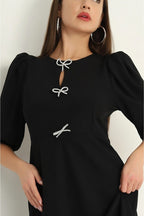 Black dress with white bow details worn by a model against a neutral background