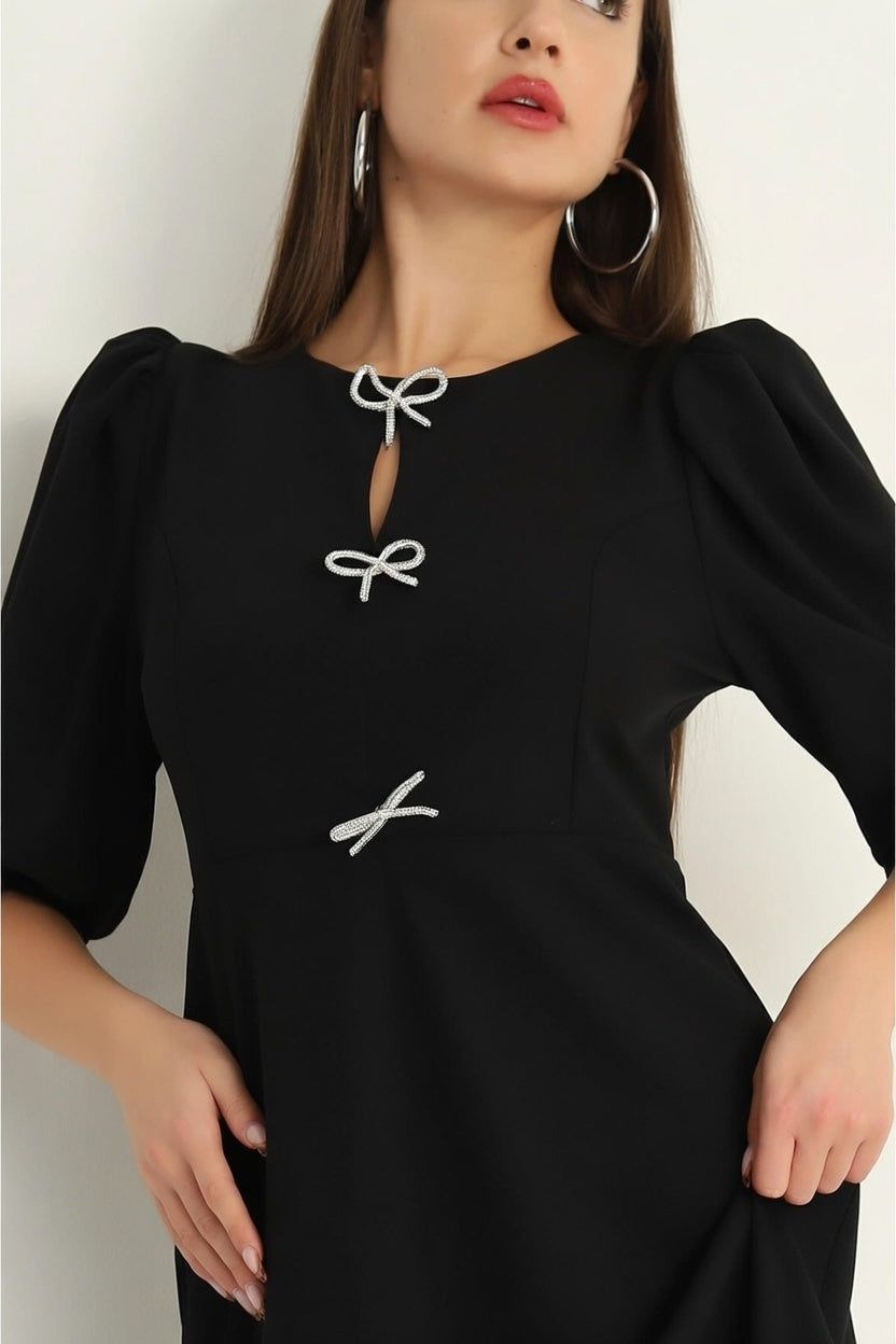 Black dress with white bow details worn by a model against a neutral background