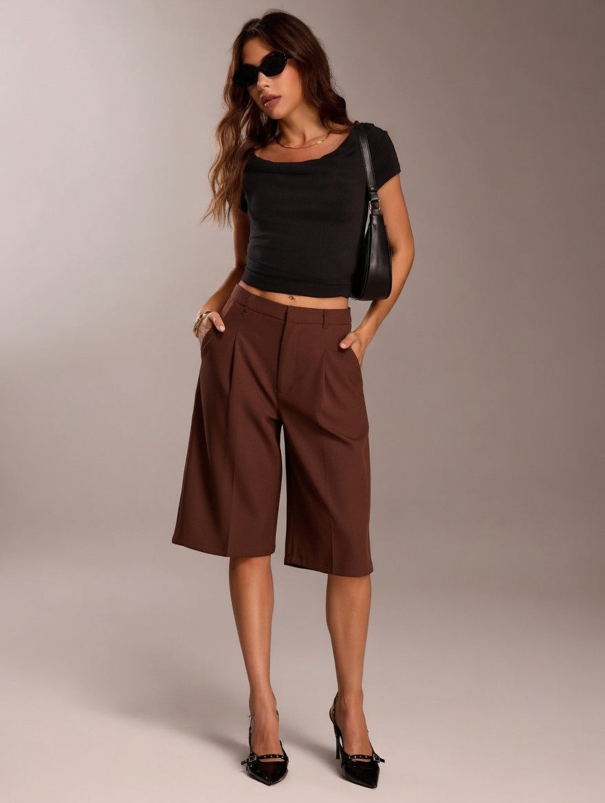 Woman wearing a black top and brown high-waisted pants against a plain background