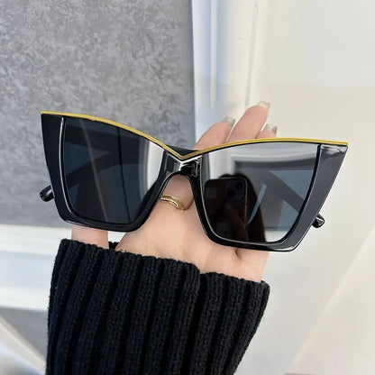 Black sunglasses with gold frame held by a hand against a neutral background