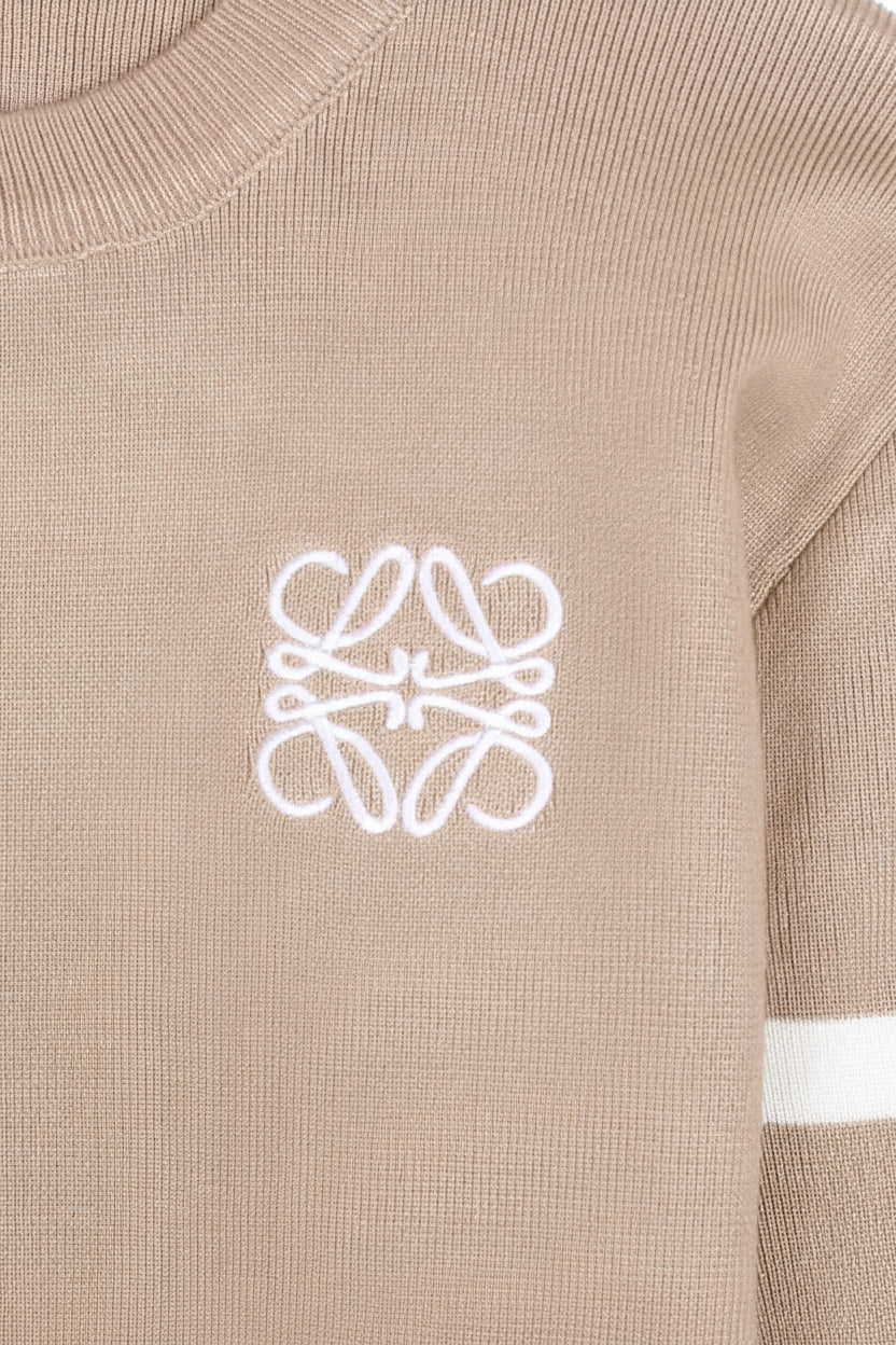 Close-up of a beige sweater with a white logo on the chest.