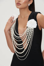 Woman wearing a black dress with white floral embellishments and layered pearl necklace.