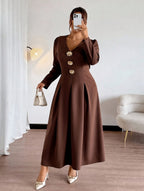 Woman wearing a brown dress with gold buttons in a room.