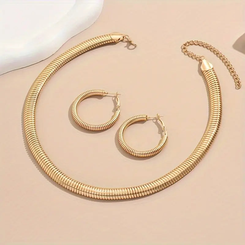 Gold necklace and hoop earrings on a beige surface