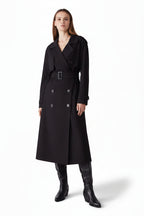 Woman wearing a black trench coat and knee-high boots on a white background