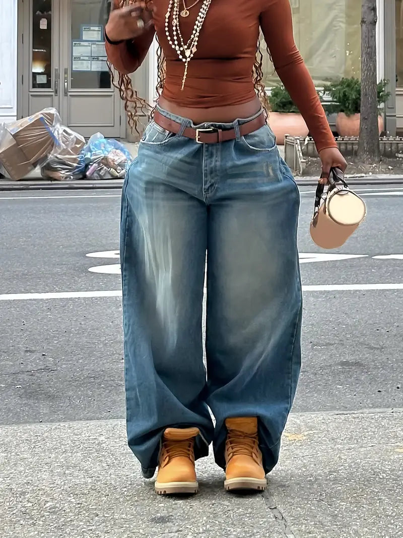 Person wearing a brown top, blue jeans, and tan boots on a street.