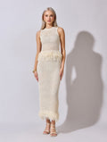 Woman wearing a white crochet dress with feather details on a plain background