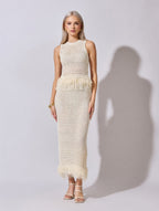 Woman wearing a white crochet dress with feather details on a plain background