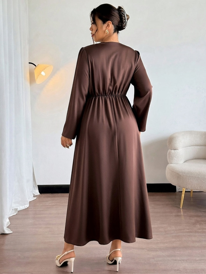 Woman wearing a brown dress in a room with a white wall and a light fixture.