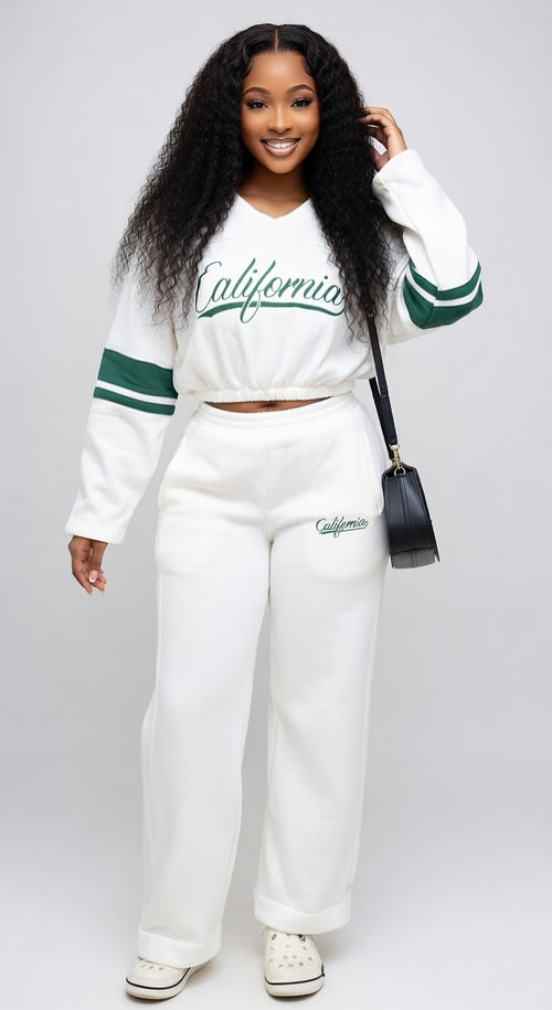 Person wearing a white 'California' sweatshirt and pants with green accents on a plain background
