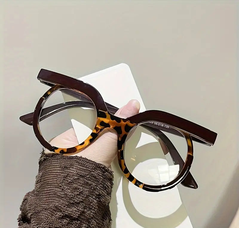 Tortoiseshell cat-eye glasses held by a hand against a neutral background