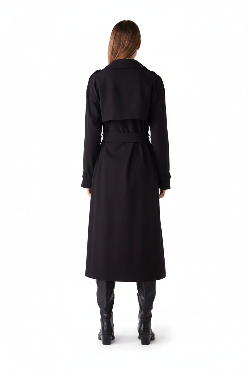 Person wearing a long black coat on a plain background