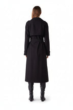 Person wearing a long black coat on a plain background