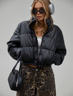 Woman wearing a black puffer jacket, leopard print pants, and headphones on a gray background