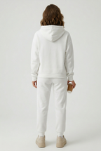 Person wearing a white hoodie and pants on a light gray background