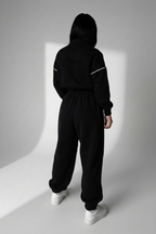Person wearing a black tracksuit with white stripes on a white background