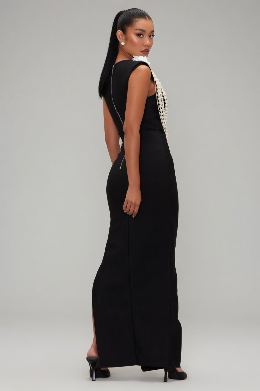 Woman wearing a black evening gown with pearl detailing on a gray background