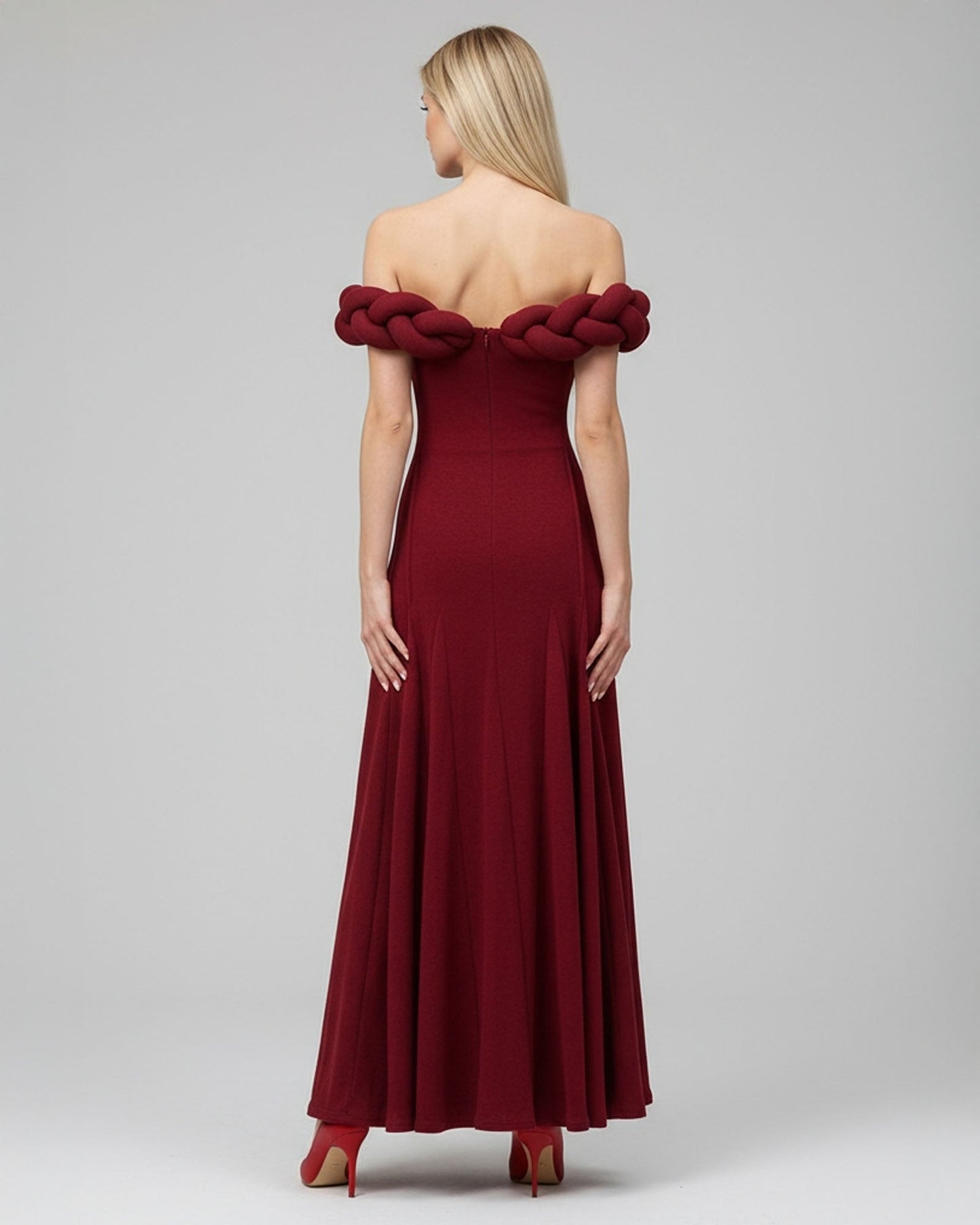 Red off-shoulder evening gown with braided detailing on a gray background