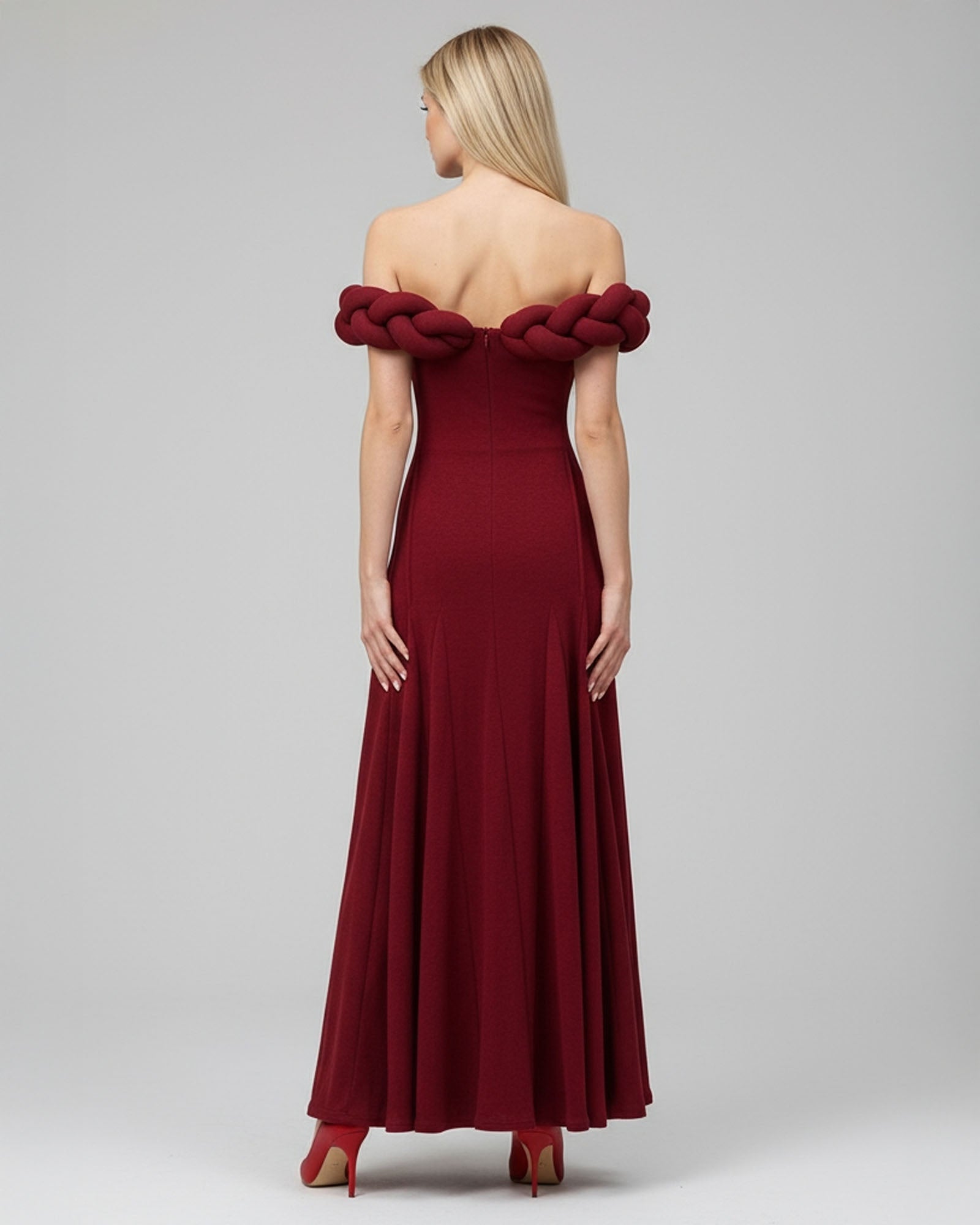 Red off-shoulder evening gown with braided detailing on a gray background