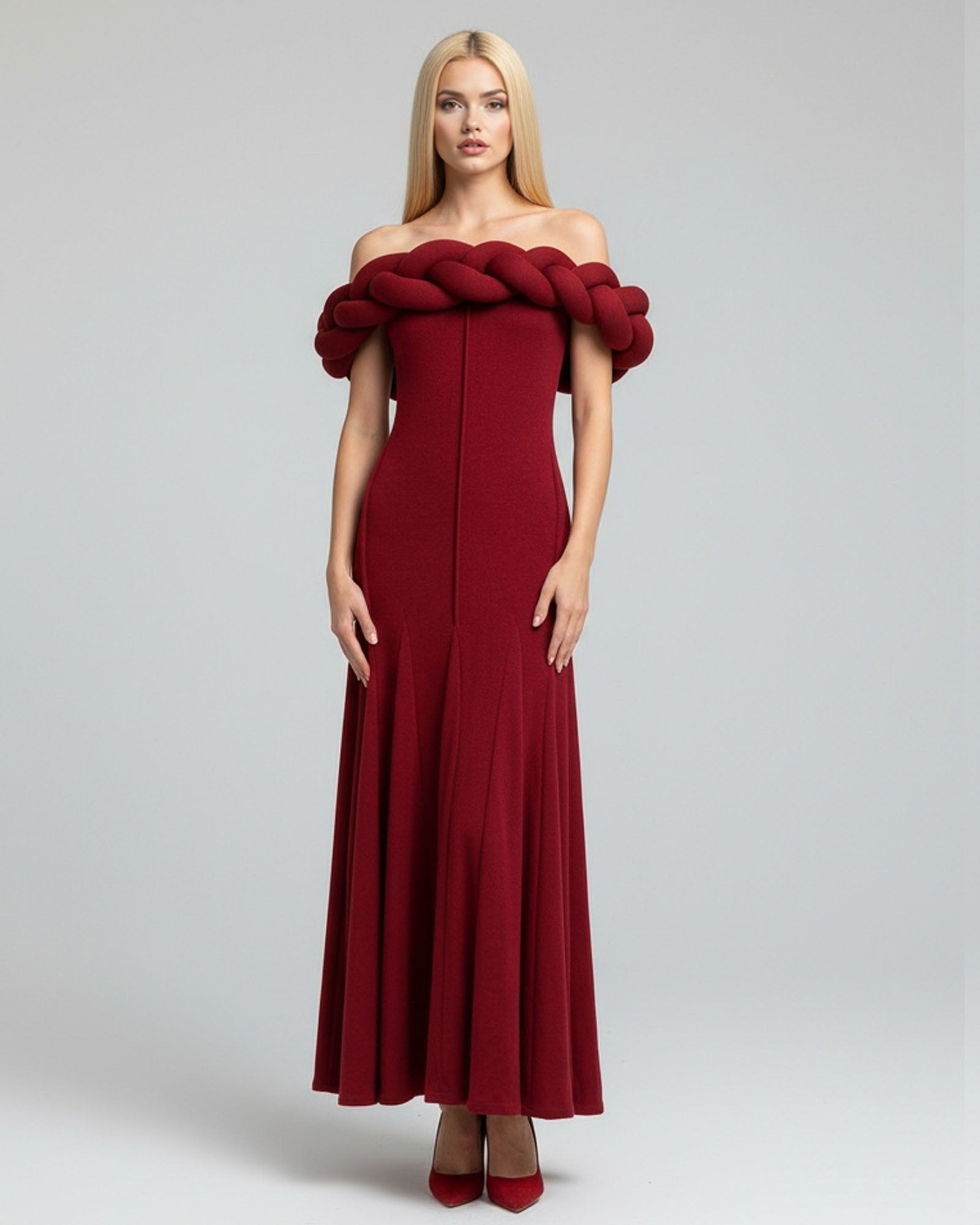 Woman wearing a burgundy off-shoulder dress with a large braided detail on a gray background