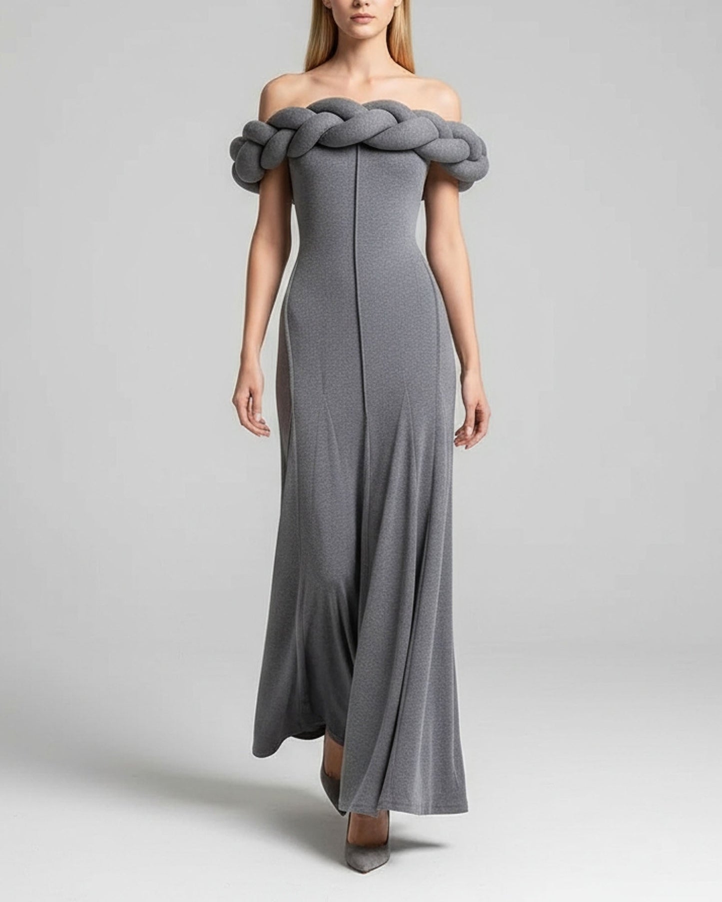 Woman wearing a gray off-shoulder dress with braided detail on a plain background