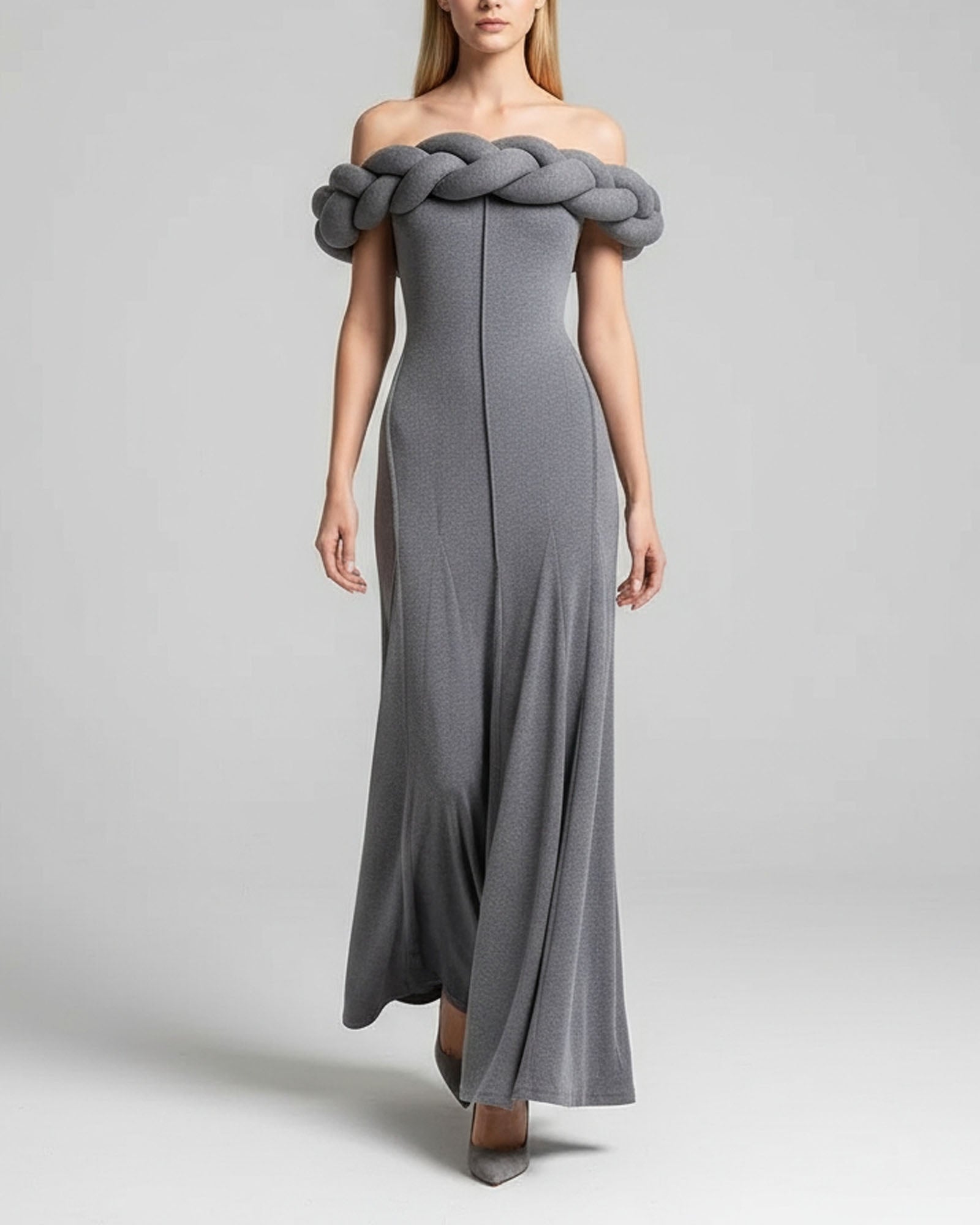 Woman wearing a gray off-shoulder dress with braided detail on a plain background