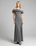 Woman wearing a gray off-shoulder dress with braided detailing on a plain background