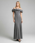 Woman wearing a gray off-shoulder dress with braided detailing on a plain background