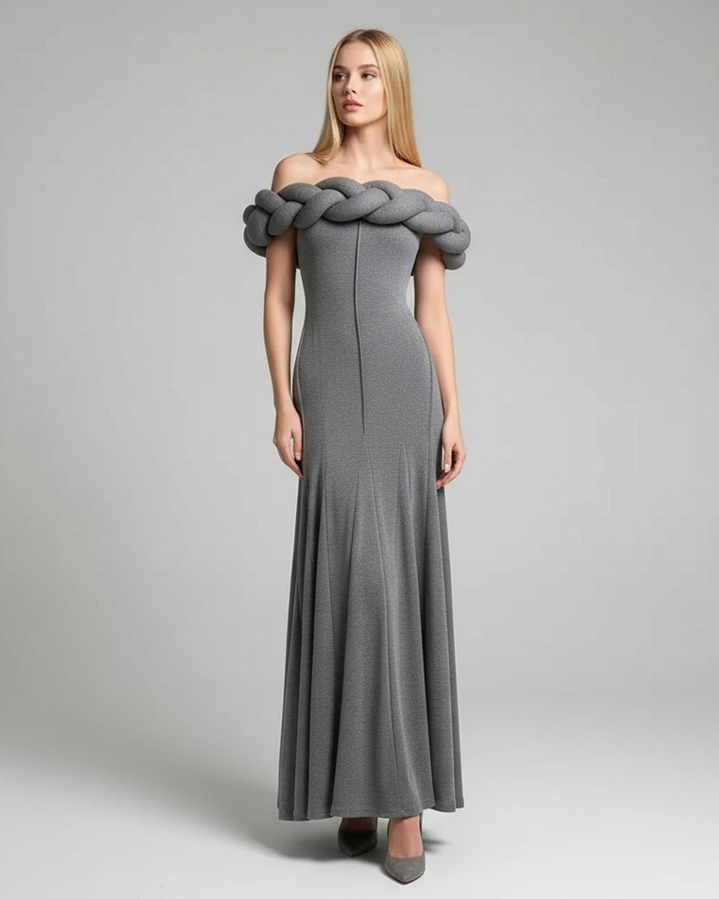 Woman wearing a gray off-shoulder dress with braided detailing on a plain background