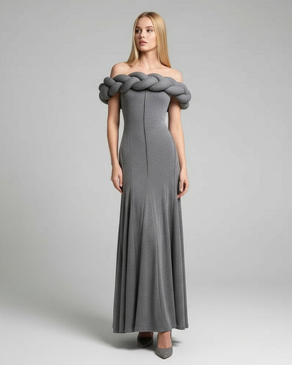 Woman wearing a gray off-shoulder dress with braided detailing on a plain background