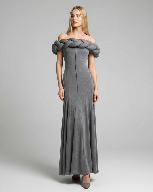 Woman wearing a gray off-shoulder dress with braided detailing on a plain background