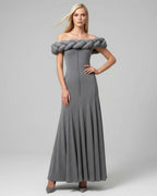 Woman wearing a gray off-shoulder dress with a large braided detail on a plain background