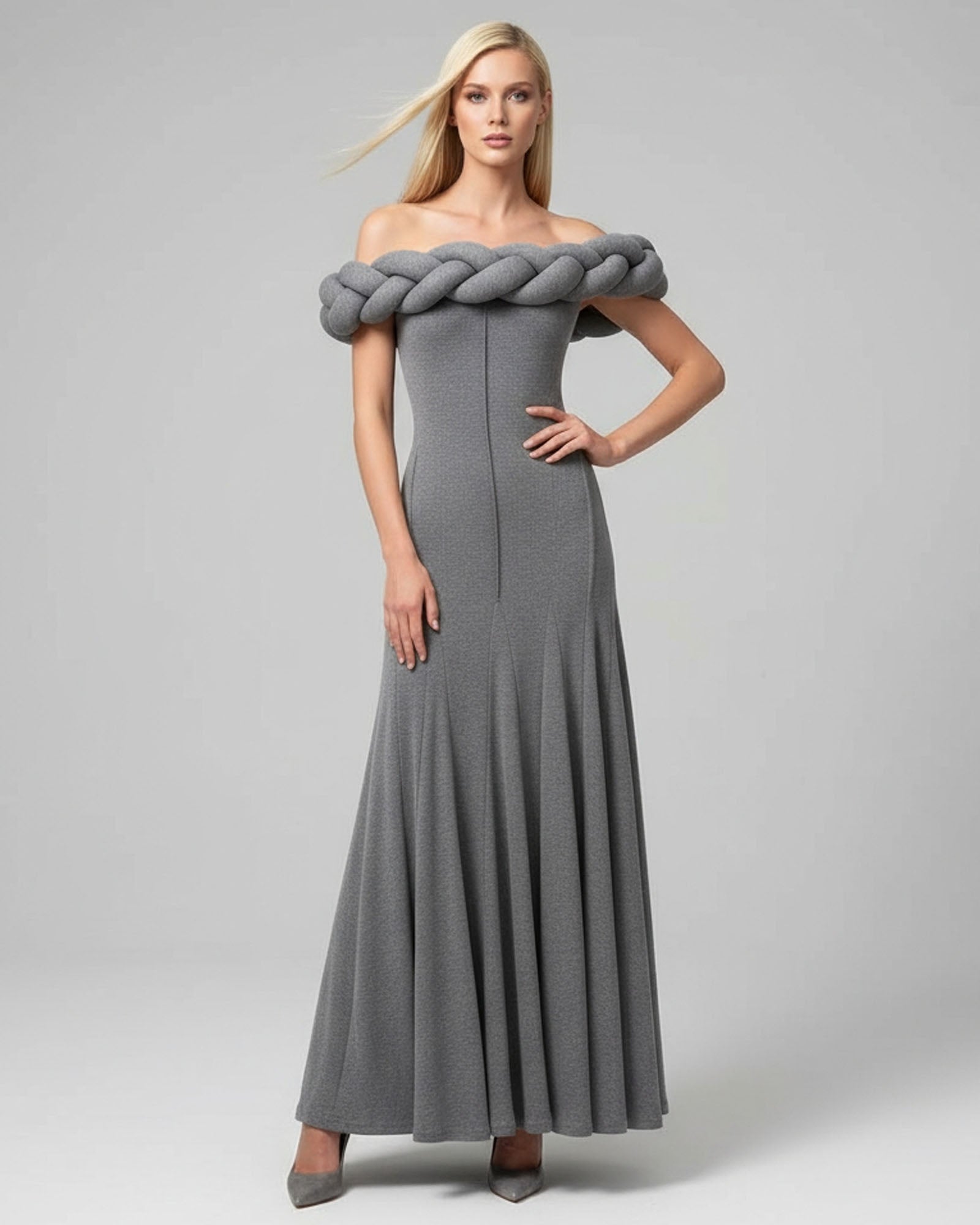 Woman wearing a gray off-shoulder dress with a large braided detail on a plain background