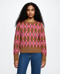 Woman wearing a brown and pink argyle sweater with blue jeans on a white background