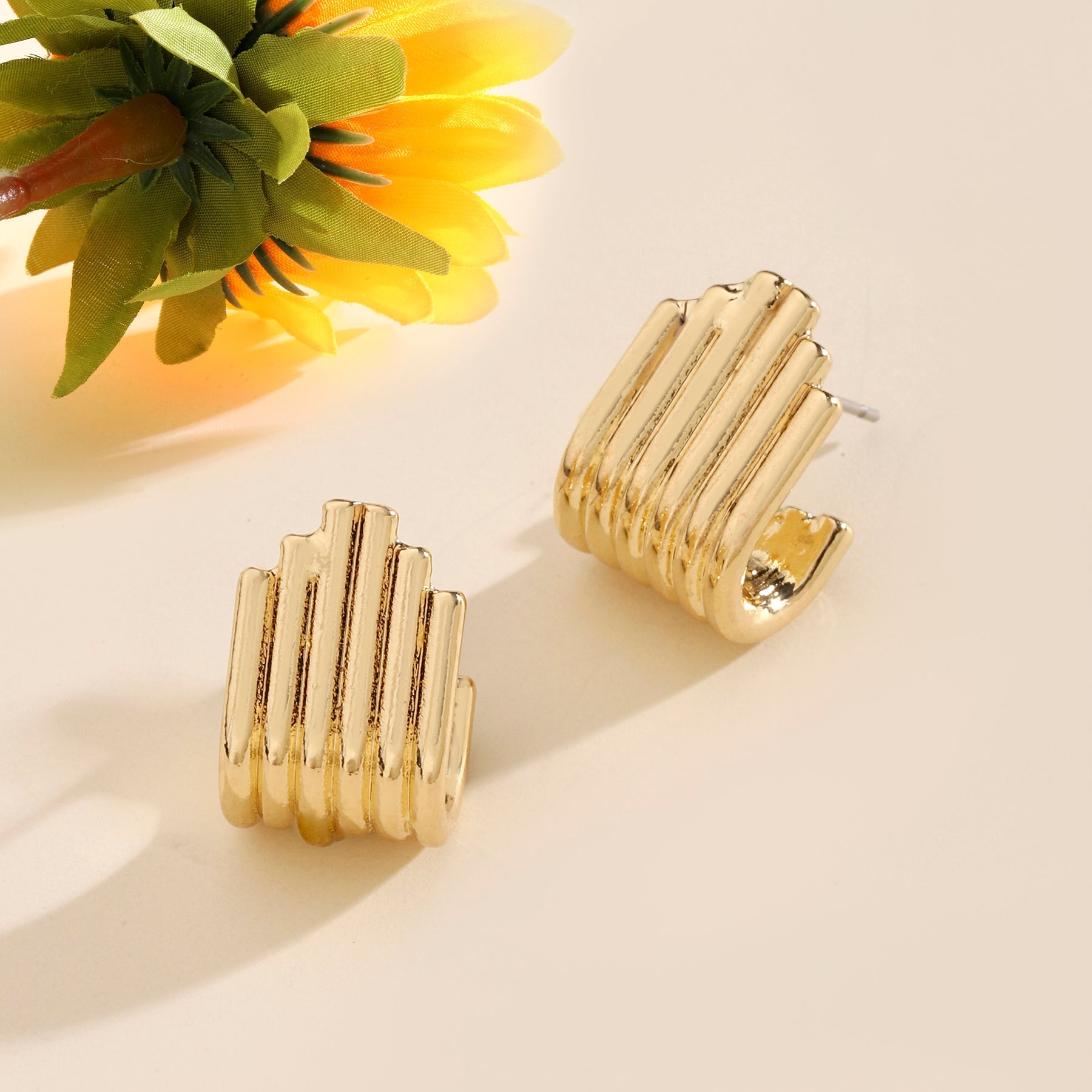Gold hoop earrings on a beige surface with a sunflower in the background