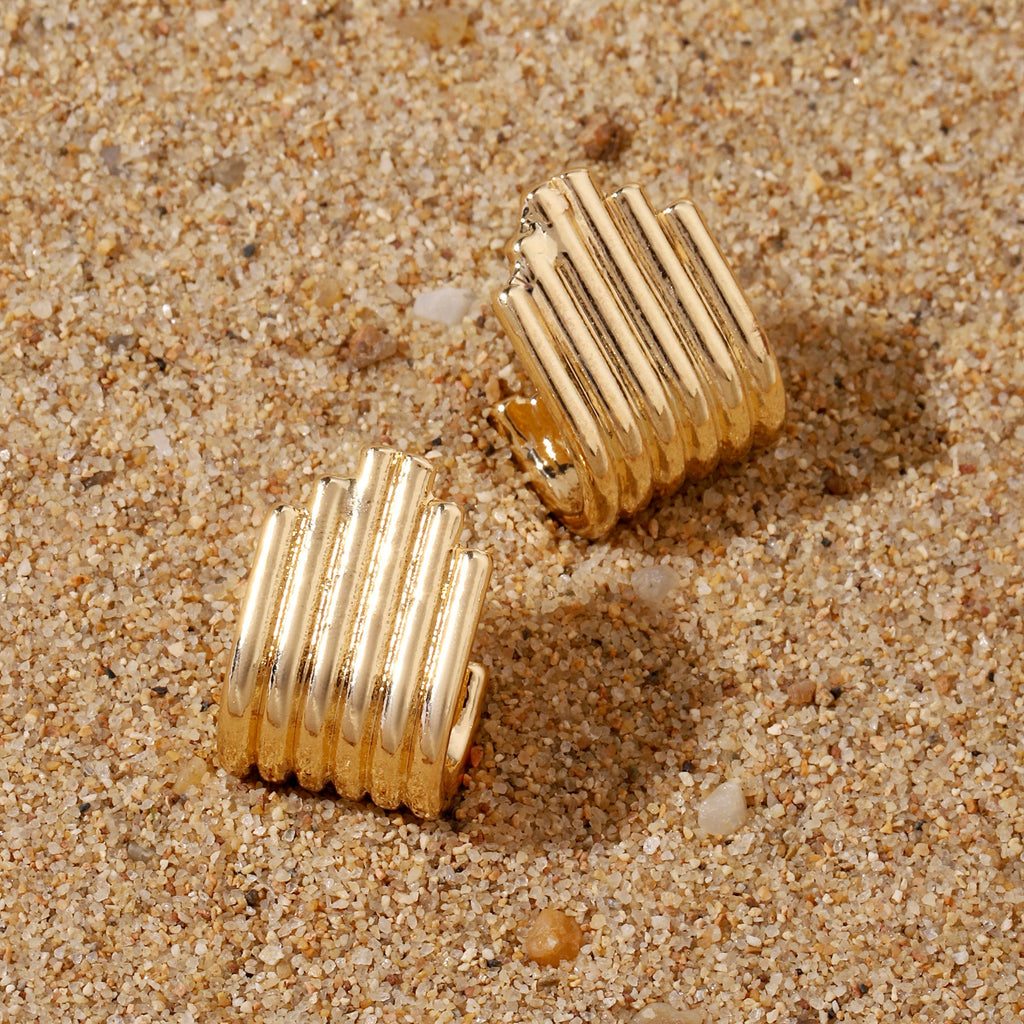 Gold ribbed earrings on a sandy surface