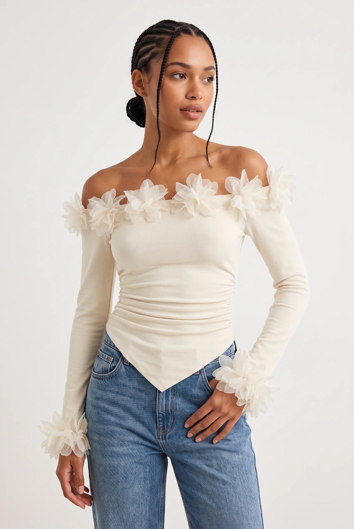 Elegant off-the-shoulder top in a soft cream hue is crafted from a smooth, form-fitting fabric with delicate ruching along the torso that accentuates the silhouette. 