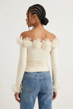 Elegant off-the-shoulder top in a soft cream hue is crafted from a smooth, form-fitting fabric with delicate ruching along the torso that accentuates the silhouette. 