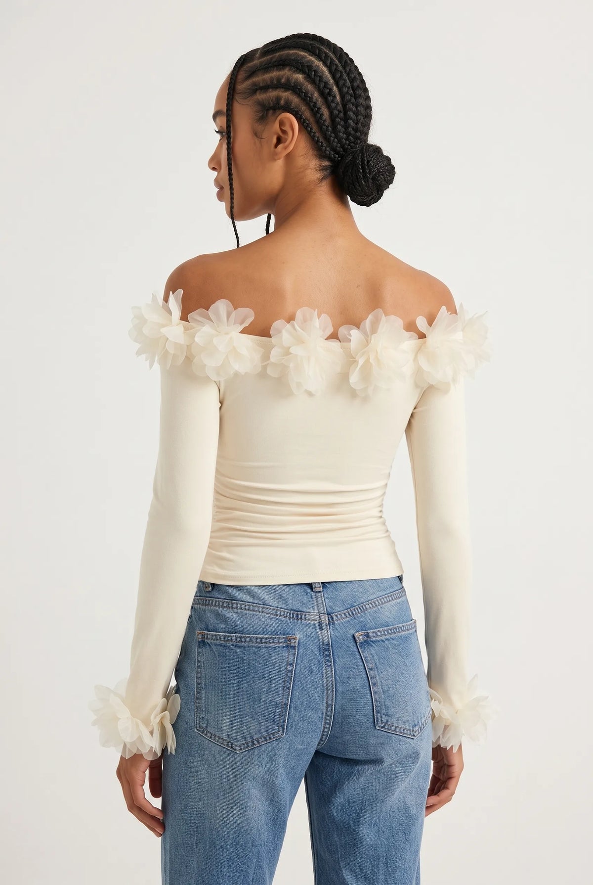 Elegant off-the-shoulder top in a soft cream hue is crafted from a smooth, form-fitting fabric with delicate ruching along the torso that accentuates the silhouette. 
