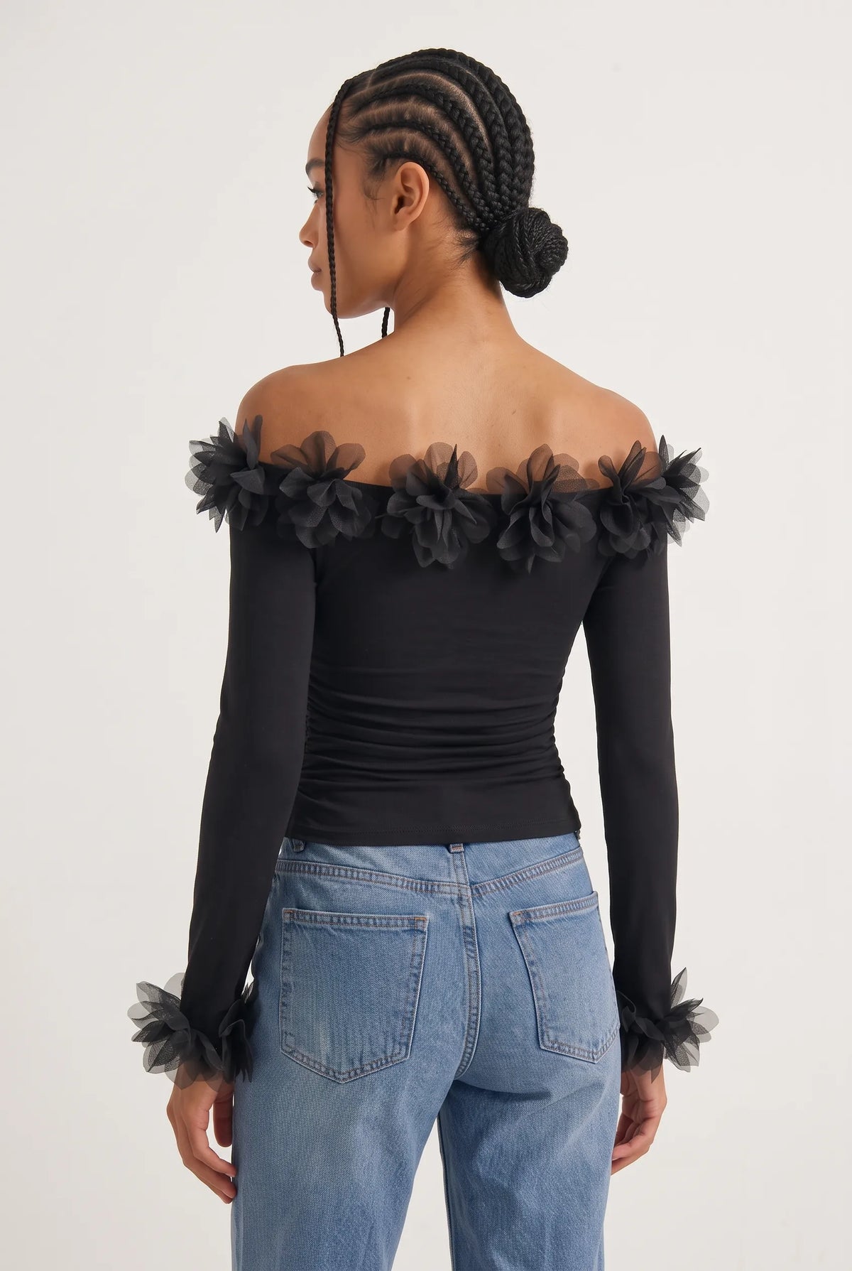 Elegant off-the-shoulder top in a soft black hue is crafted from a smooth, form-fitting fabric with delicate ruching along the torso that accentuates the silhouette. 