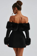 Woman wearing a black dress with fur sleeves against a gray background