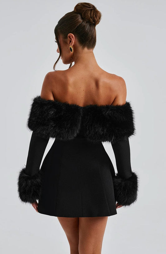 Woman wearing a black dress with fur sleeves against a gray background