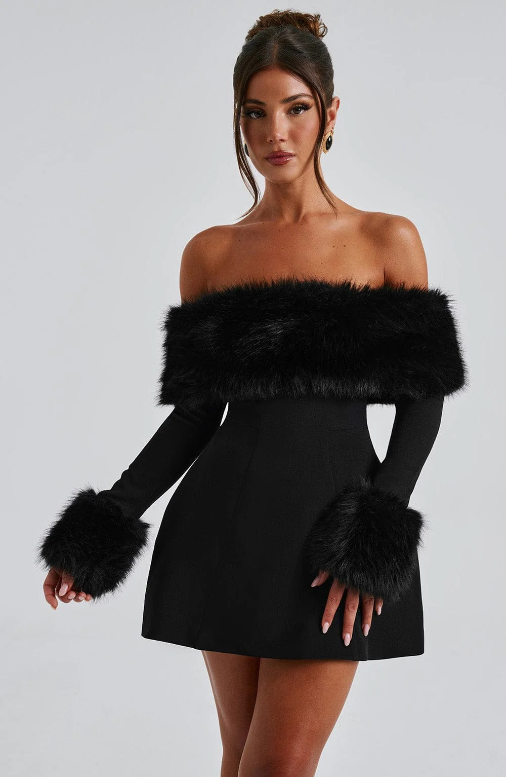 Woman wearing a black off-shoulder dress with fur accents on a gray background