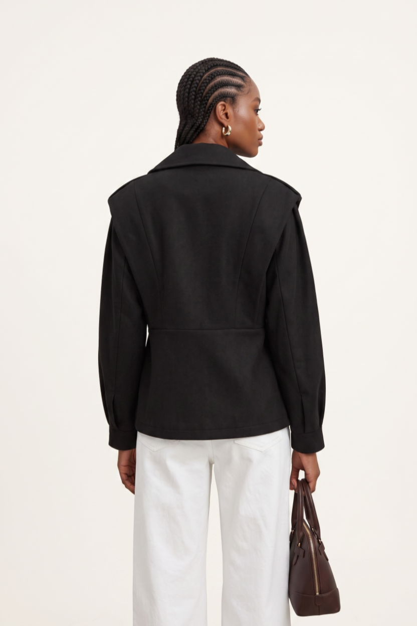Person wearing a black jacket and white pants, holding a brown bag on a light background