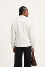 Person wearing a white jacket and black pants holding a brown bag on a white background