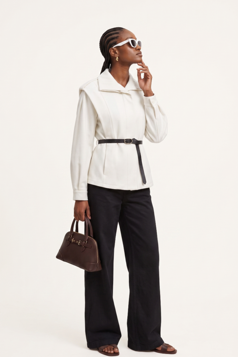 Woman wearing a white jacket and black pants, holding a brown handbag on a white background