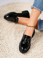 Black glossy loafers worn with denim jeans on a textured beige surface