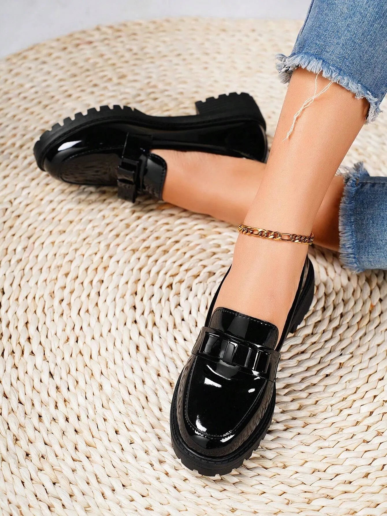 Black glossy loafers worn with denim jeans on a textured beige surface