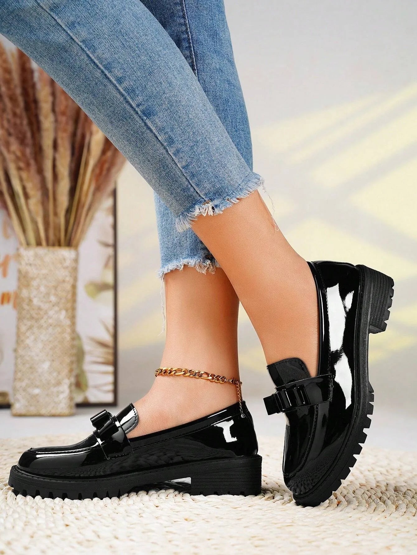 Black patent leather shoes worn with light blue jeans on a neutral background