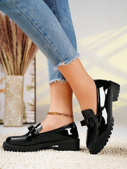 Black patent leather shoes worn with light blue jeans on a neutral background